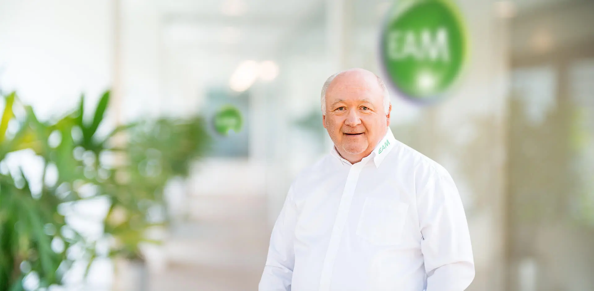 Ein lachender Mann steht vor einem EAM-Logo in einem Büro.