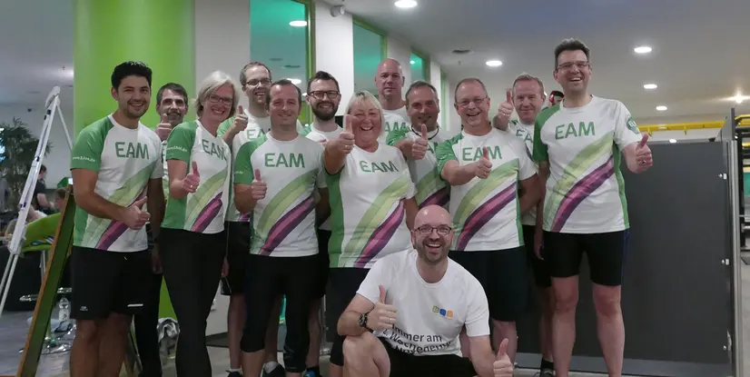 Gruppe von Personen in sportlichen T-Shirts, die Daumen hoch zeigen, in einem Fitnessstudio.