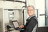 Bau und Betrieb von Messstellen Techniker mit Laptop vor einem Schaltschrank, lächelnd und bei der Arbeit an elektrischen Geräten.
