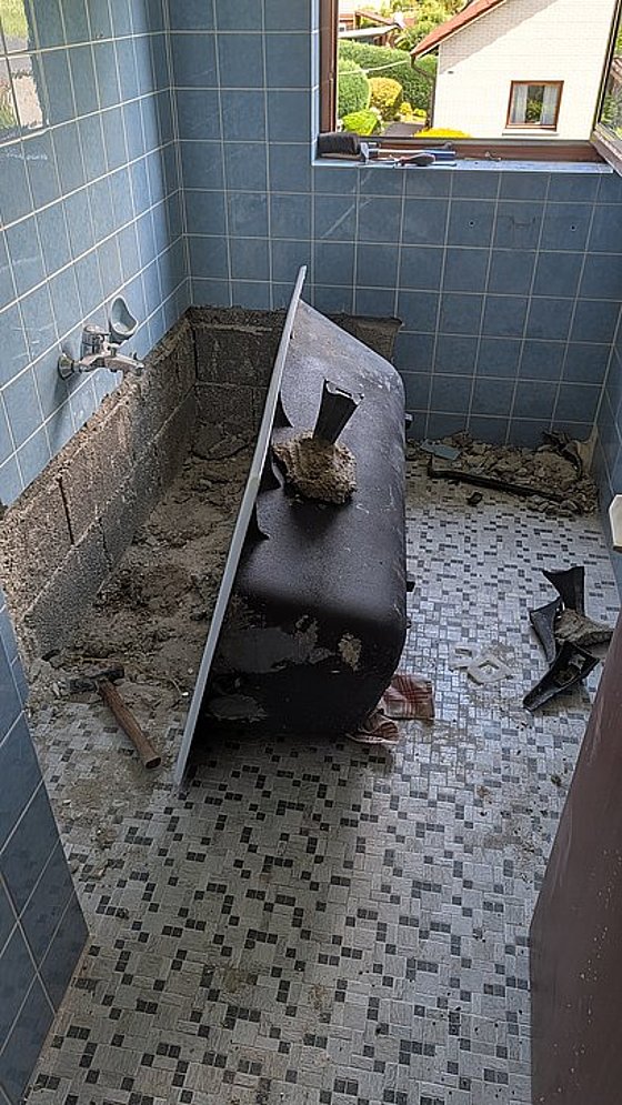 Ein Badezimmer mit einer umgestürzten Badewanne, sichtbarem Untergrund und blauen Fliesen an den Wänden.