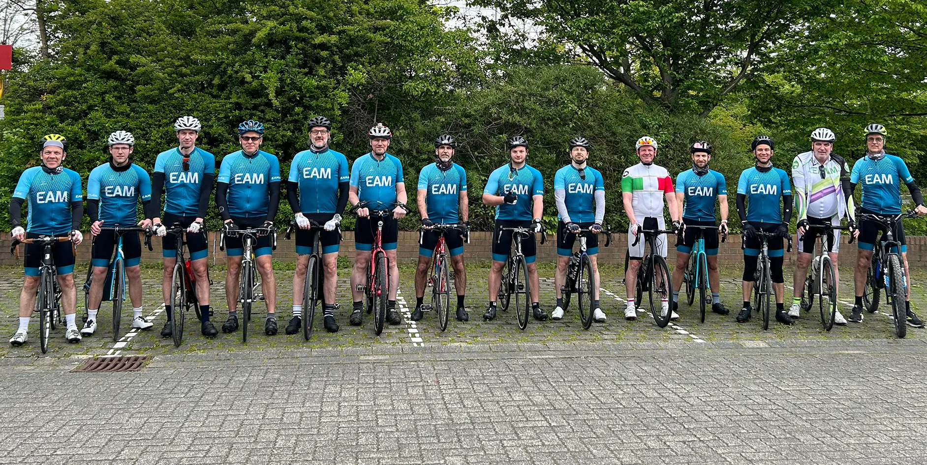 Gruppe von Radfahrern in blauer Teamsportkleidung, stehend neben ihren Fahrrädern, lächelnd in einer natürlichen Umgebung.