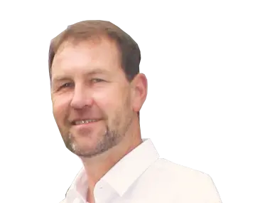 Markus Schuchart Portrait eines Mannes mit Bart, in weißem Hemd, lächelnd vor neutralem Hintergrund.