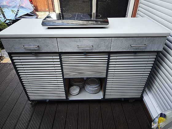 Küchenwagen mit induktiver Kochplatte, drei Schubladen und offenem Fach für Geschirr im unteren Bereich.