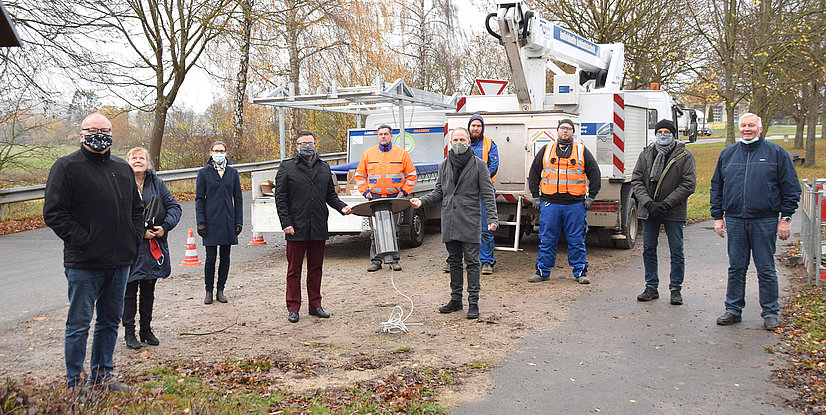 Eine Gruppe von Personen steht auf einem Weg neben einem Arbeitsfahrzeug und hält einen Laternenkopf in der Hand.