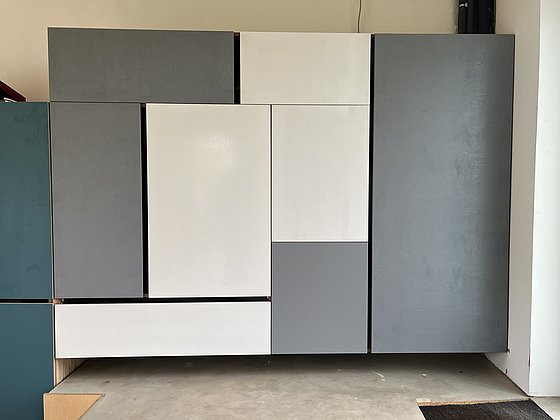 Moderner Schrank mit grauen, weißen und blauen Flächen in abstraktem Design, an einer Wand aufgestellt.