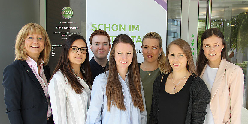 Gruppe von sieben Personen vor dem EAM Energie GmbH Gebäude, freundlich lächelnd, mit klarer Sicht auf das Logo im Hintergrund.