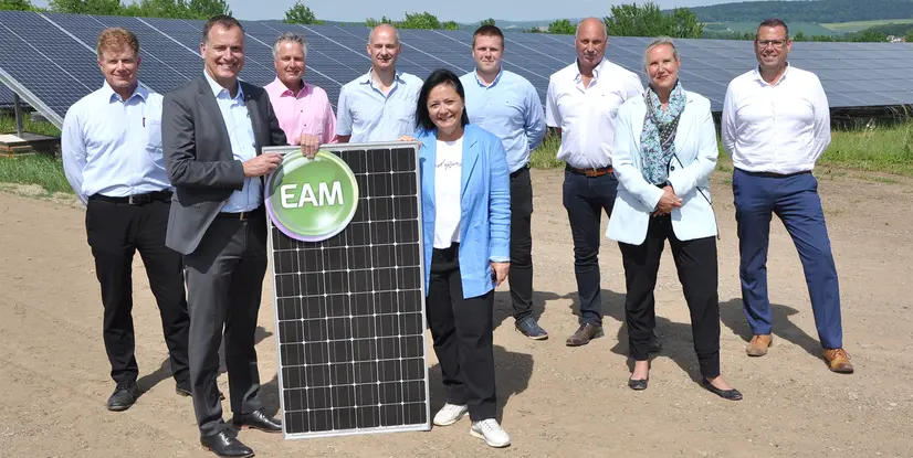 Gruppenzusammenkunft von Fachleuten vor einer Solaranlage mit einem Solarpanel und dem Logo EAM.