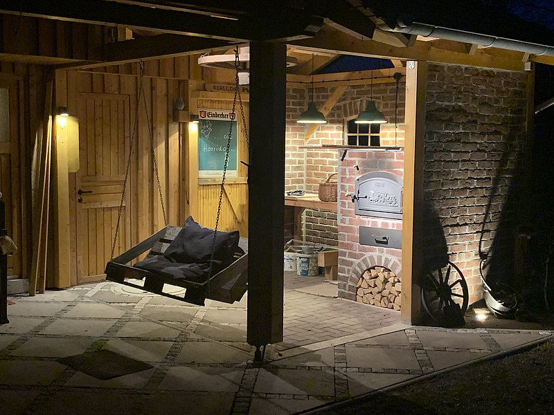 Holzhütte bei Nacht mit einer Schaukel, Steinofen und warmem Licht, rustikale Atmosphäre und gemütliche Ecke.