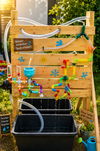 Wasser-Spielstation mit bunten Rohren, Spritzern und Behälter; für Kinder zum Lernen und Entdecken.