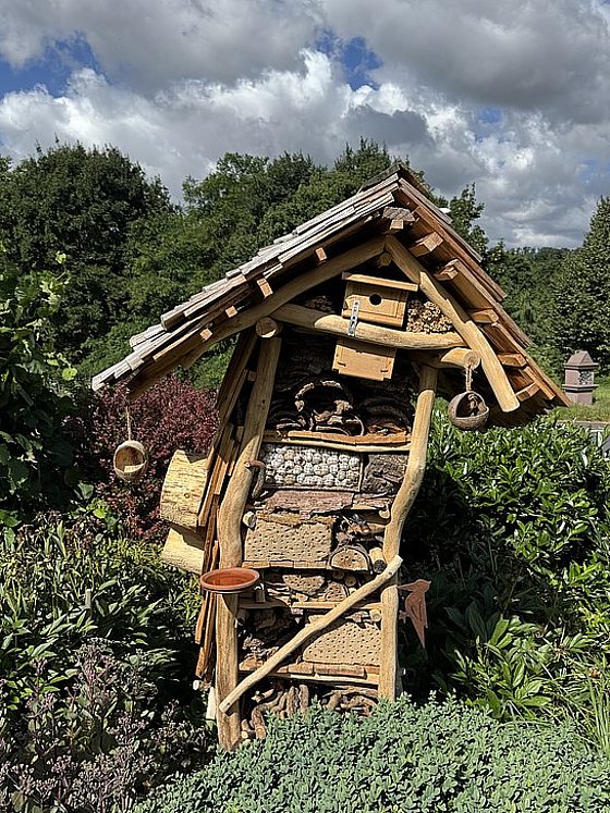 Ein Insektenhotel aus Holz mit Dach, gefüllt mit natürlichen Materialien, um nützliche Insekten zu fördern, umgeben von Pflanzen.