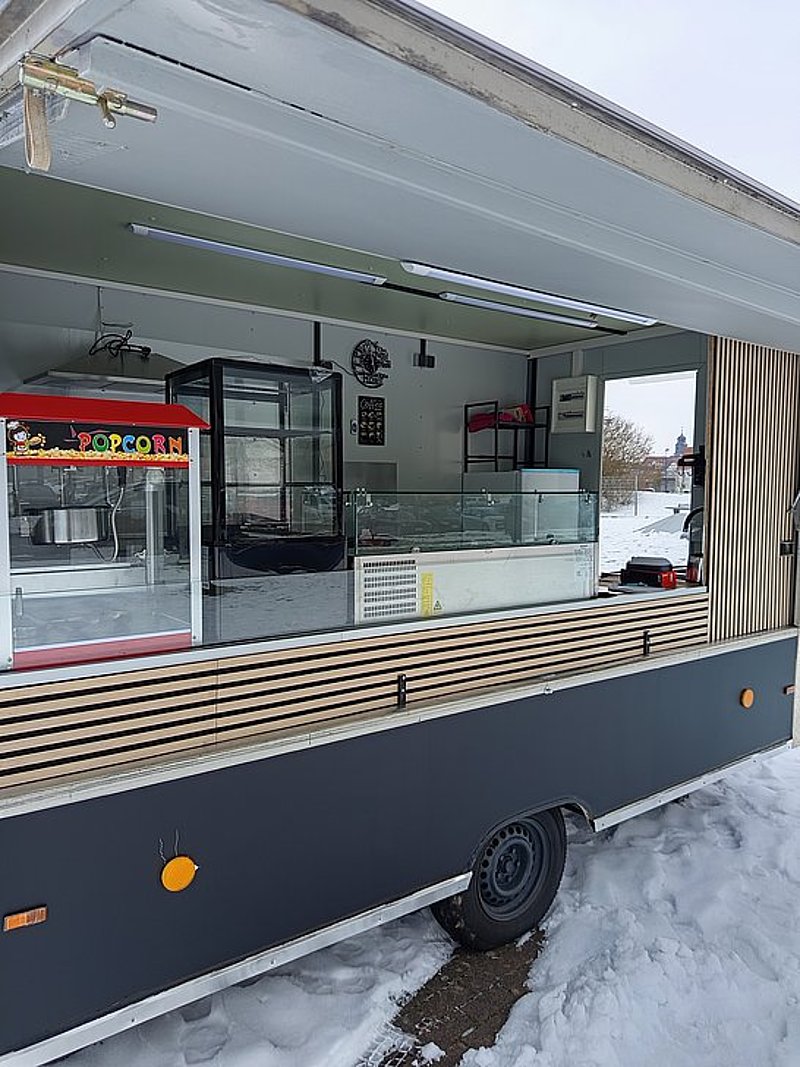 Ein Mobiler Verkaufsstand im Winter, mit Vitrine, Popcornmaschine und Schneedecke darunter.