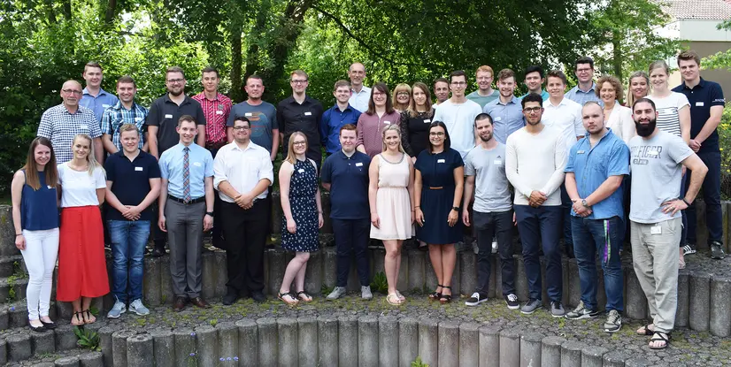 Gruppenfoto von 41 Personen, die auf einer Treppe im Freien stehen, umgeben von Bäumen und Grünflächen.