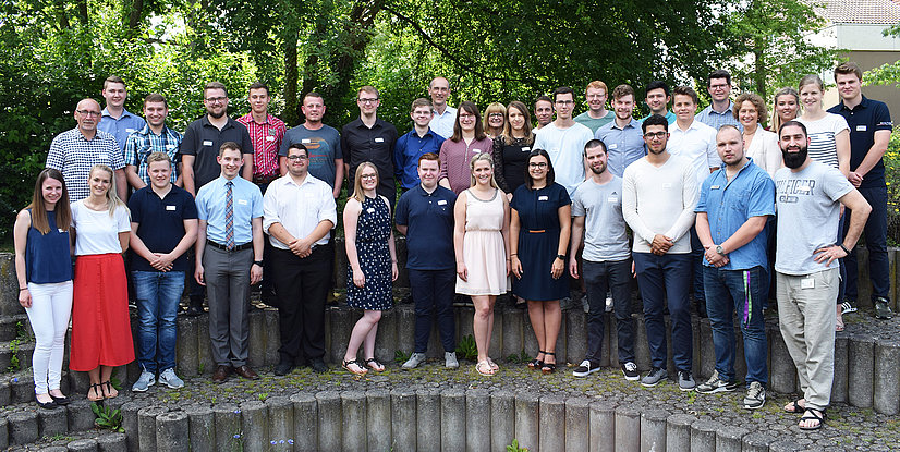 Gruppenfoto von 41 Personen, die auf einer Treppe im Freien stehen, umgeben von Bäumen und Grünflächen.