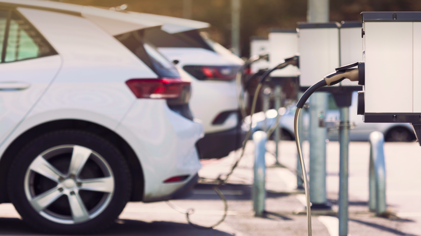 E-Ladestationen auf einem Parkplatz mit geparkten Elektrofahrzeugen im Hintergrund.