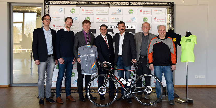 Gruppennfoto von sieben Personen mit einem Fahrrad und Sportbekleidung, präsentiert bei einer Veranstaltung in Göttingen.