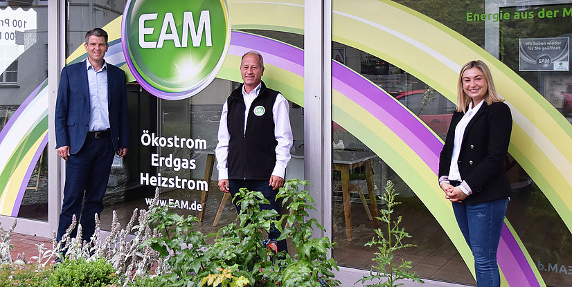Drei Personen stehen vor dem EAM-Kundenservicebüro in Solms, das mit bunten Farben und Logos dekoriert ist.