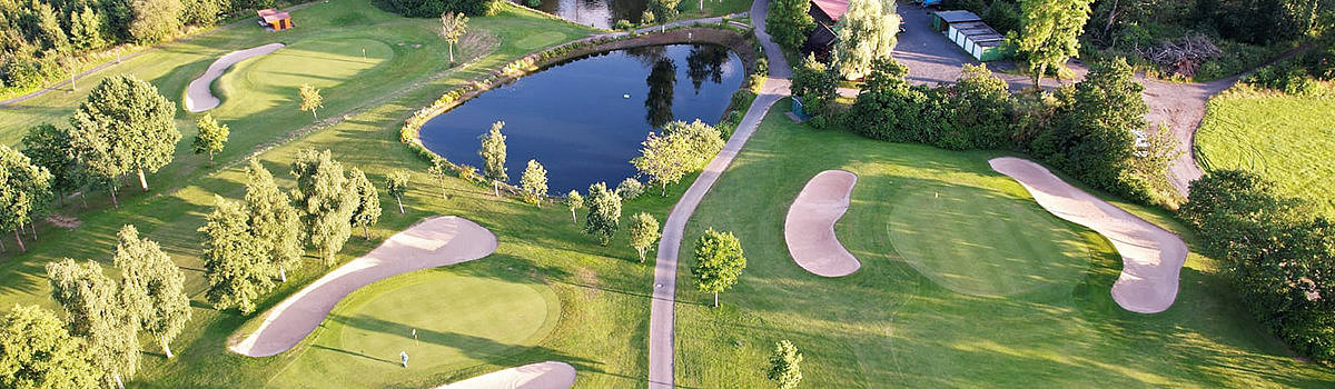 Luftaufnahme eines Golfplatzes mit Sandbunkern, einem Teich und umgebenden Bäumen in einer grünen Landschaft.