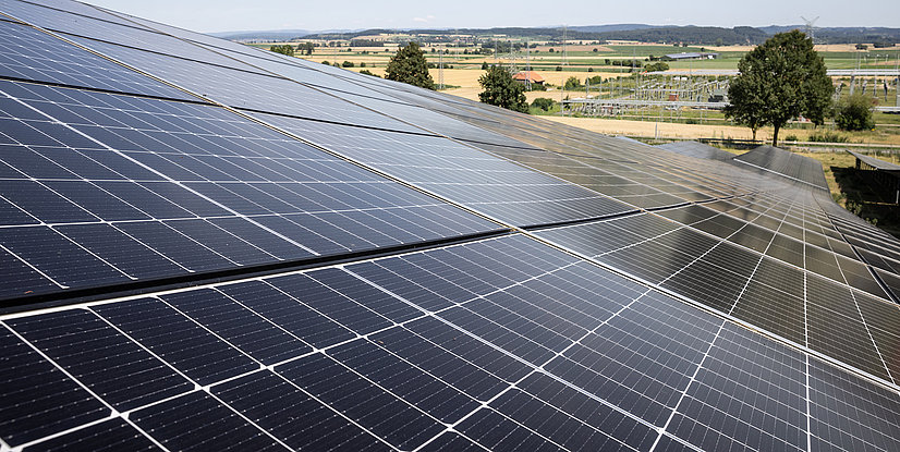 Solaranlage auf einem Dach, mit mehreren Solarzellen, im Hintergrund eine ländliche Landschaft.