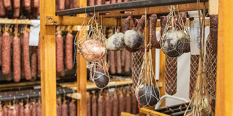 Regal mit verschiedenen sortierten Wurstwaren, darunter hängen mehrere runde Wurststücke in Netzen.