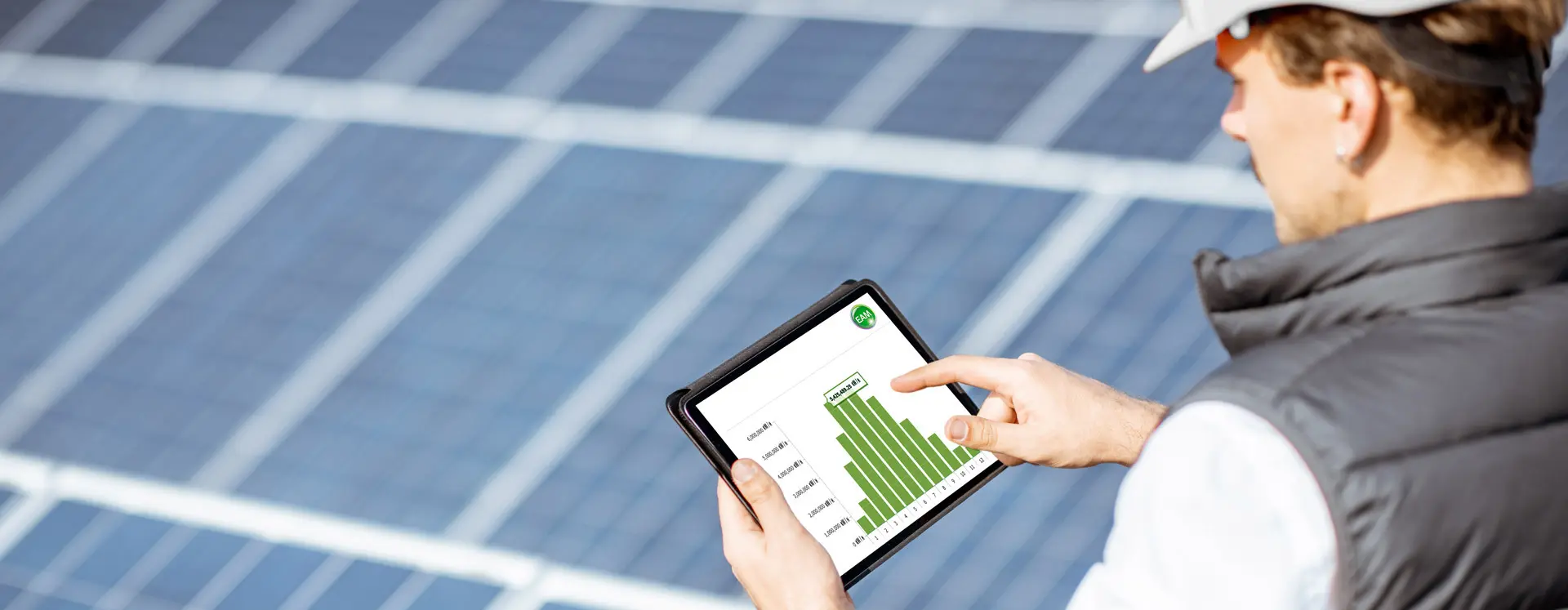 Ein Monteur mit Schutzhelm überprüft auf einem Tablet Daten vor dem Hintergrund von Solarmodulen.