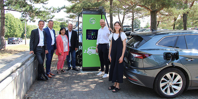 Gruppe von sechs Personen steht neben einer Elektro-Ladestation für Autos mit umweltfreundlichem Design.
