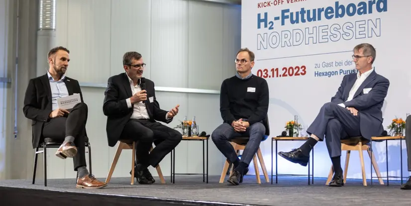 Diskussionsteilnehmer auf einer Bühne während der Veranstaltung H2-Futureboard Nordhessen, mit Stühlen und Tischen, moderner Raum.