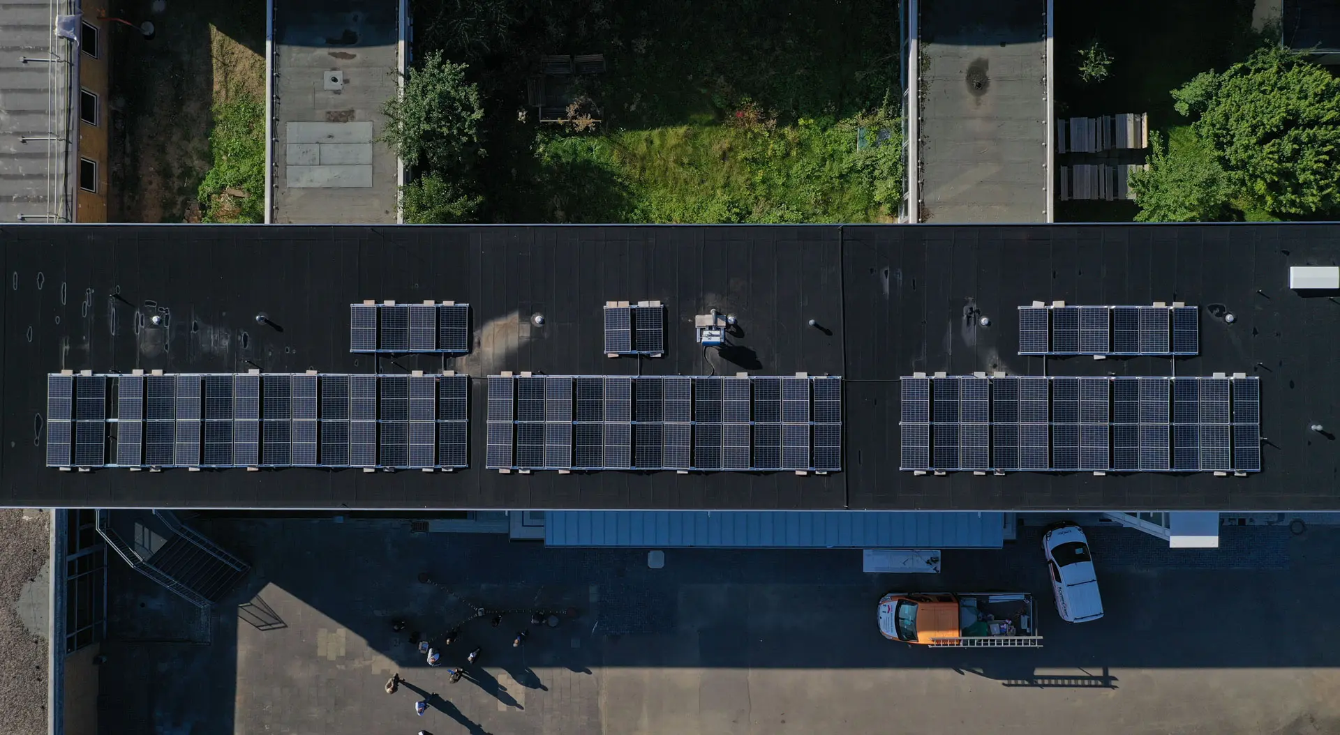 Dachansicht eines Gebäudes mit mehreren Solarzellen, darunter ein Parkplatz mit Fahrzeugen und Menschen.