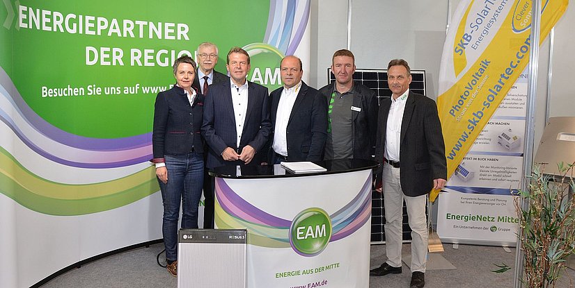 Auf einem Messestand stehen fünf Männer und eine Frau vor einem EAM-Pult, Solarmodulen und einer Werbewand mit dem Text Energiepartner der Region.