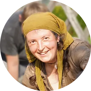 Lächelnde Frau mit Kopftuch, sitzt im Freien und arbeitet an einem Projekt. Hintergrund mit verschwommenen Personen.