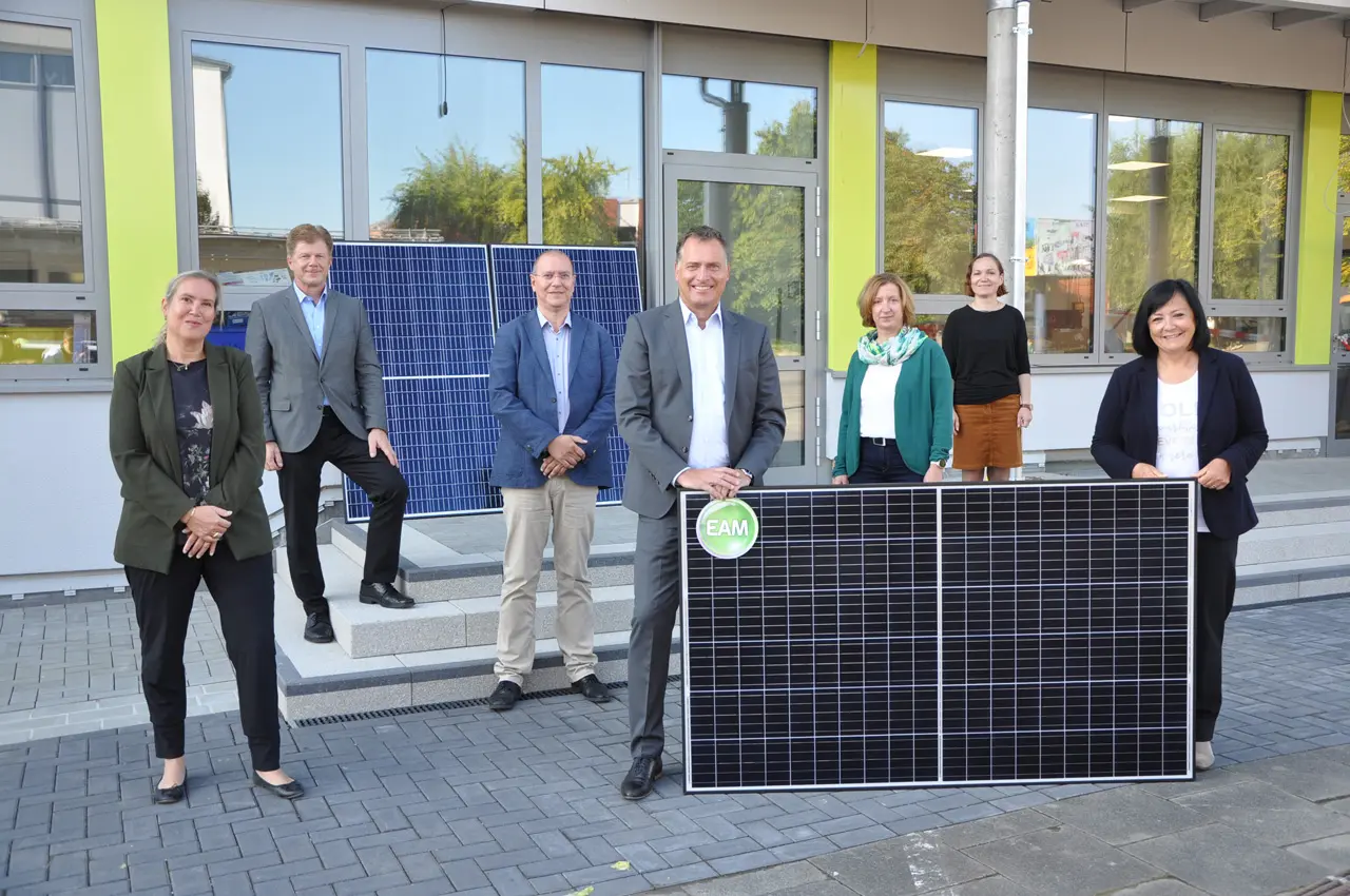 Gruppenfoto von Personen vor einem Gebäude mit Solarpanelen; es werden erneuerbare Energien thematisiert.
