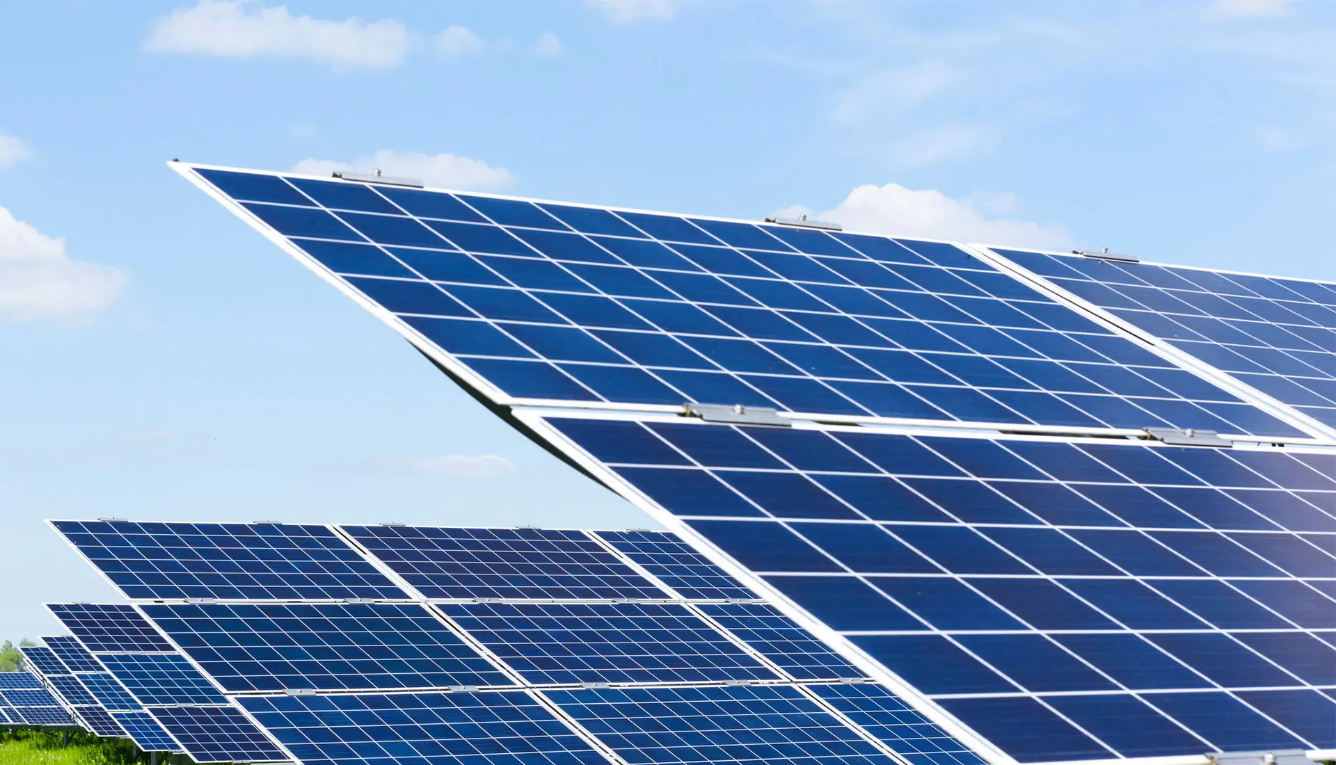 Solarpanels stehen auf einem grünen Feld unter blauem Himmel mit einigen Wolken.