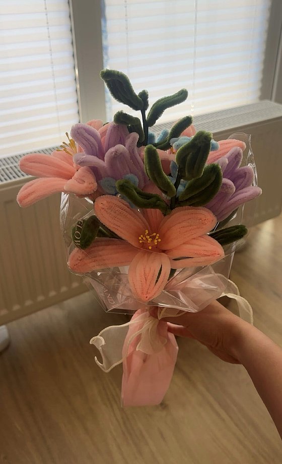 Ein buntes Blumenbouquet aus Stoff mit zarten Blüten in Rosa, Violett und Blau, verpackt in transparentem Folie.