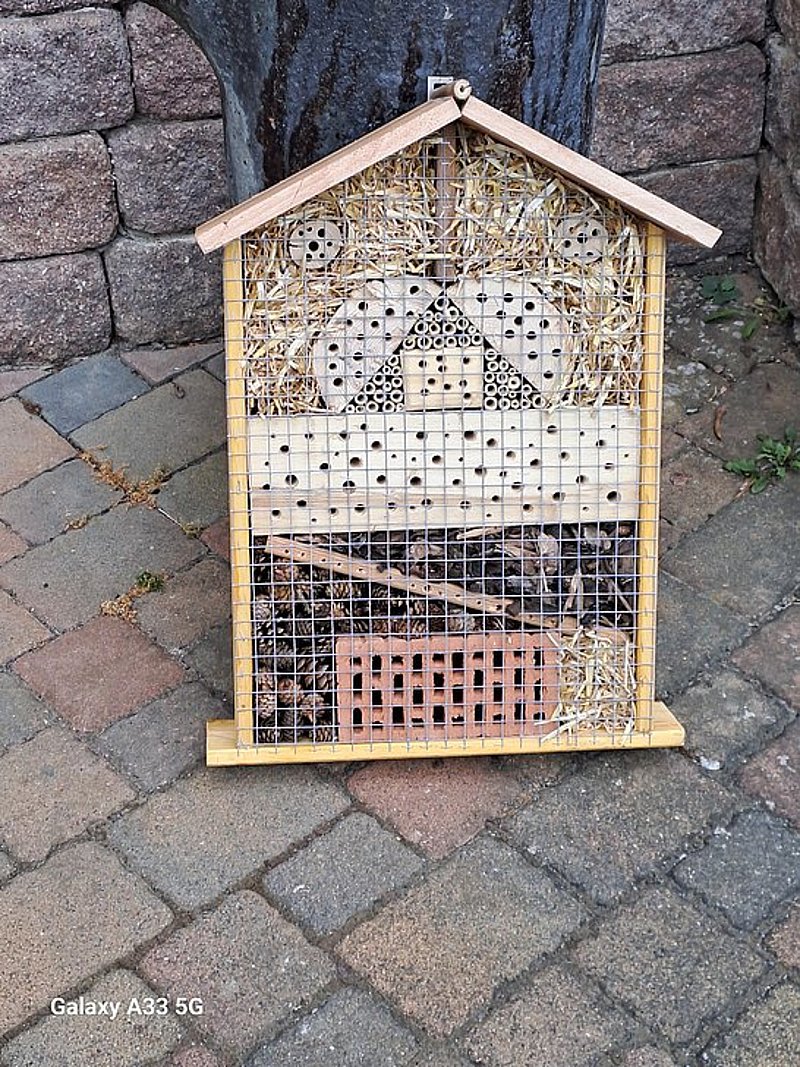 Insektenhotel mit verschiedenen Materialien zur Förderung der Biodiversität, auf einem gepflasterten Boden aufgestellt.
