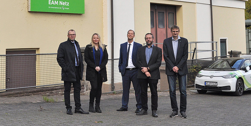 Fünf Personen stehen vor einem Gebäude mit einem Schild EAM Netz
