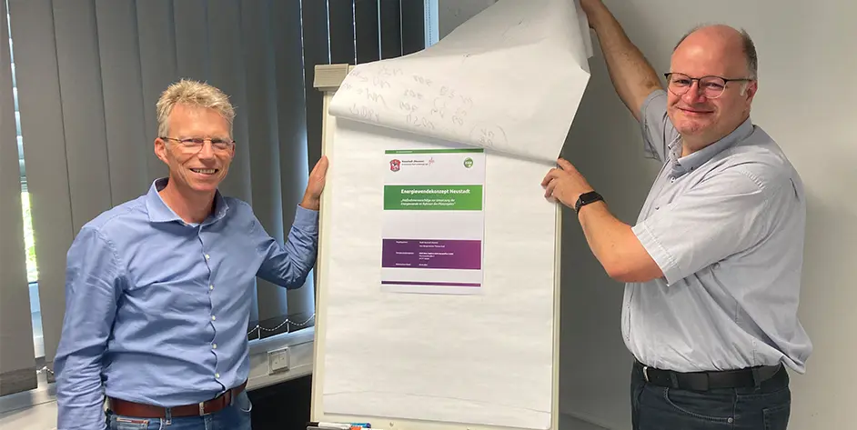 Zwei Personen lächeln, während sie ein Plakat mit dem Titel "Energiewendekonzept Neusalz"" enthüllen."