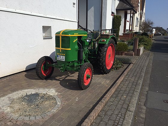 Ein farbenfroher Traktor der Marke Deutz steht an einer gepflasterten Straße neben einem weißen Gebäude.