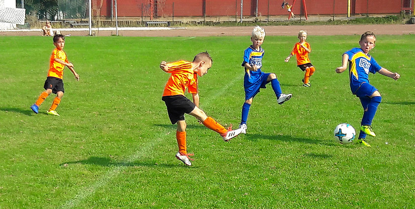 Vier Kinder spielen Fußball auf einem grünen Rasenplatz, einige treten den Ball in verschiedenen Bewegungen.