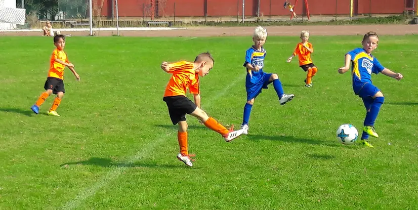 Vier Kinder spielen Fußball auf einem grünen Rasenplatz, einige treten den Ball in verschiedenen Bewegungen.