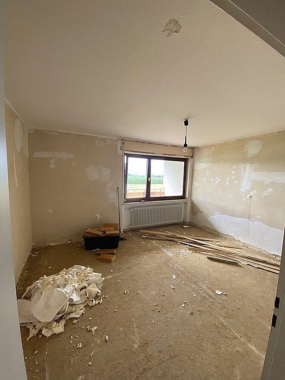 Ein unrenovierter Raum mit einem Fenster, Holzresten und einem Berg aus Sanierungsabfällen auf dem Boden.