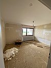 Ein unrenovierter Raum mit einem Fenster, Holzresten und einem Berg aus Sanierungsabfällen auf dem Boden.