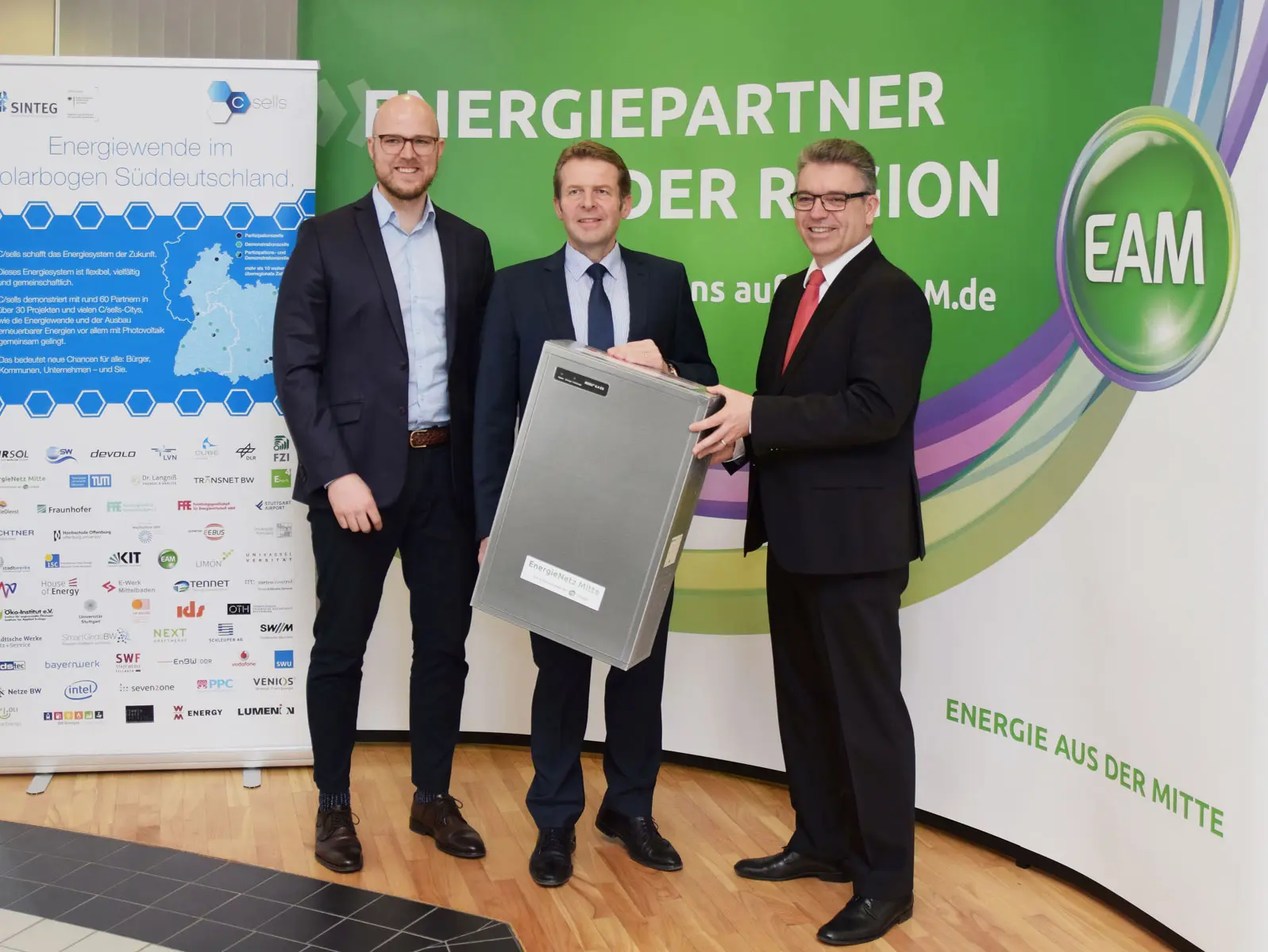 Drei Männer präsentieren eine Energiebox vor einem Banner mit dem Schriftzug "Energiepartner der Region""."