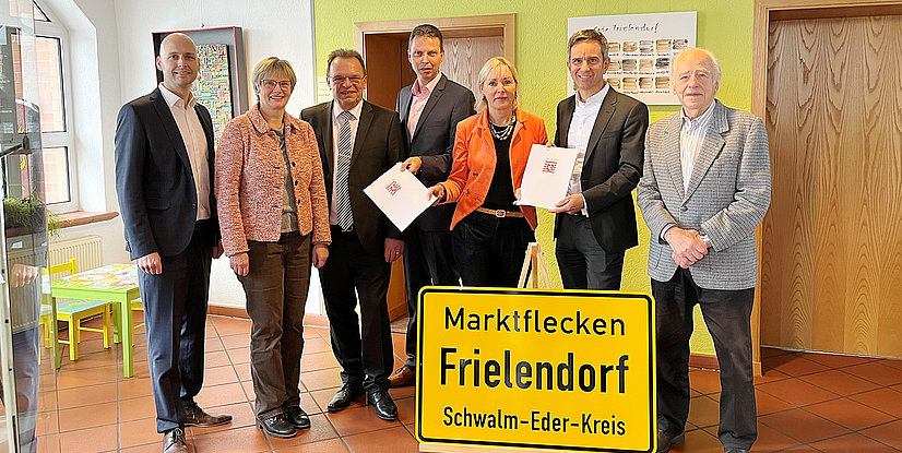 Eine Gruppe von sieben Personen steht neben einem Schild mit der Aufschrift Marktflächen Frielendorf, Schwalm-Eder-Kreis.