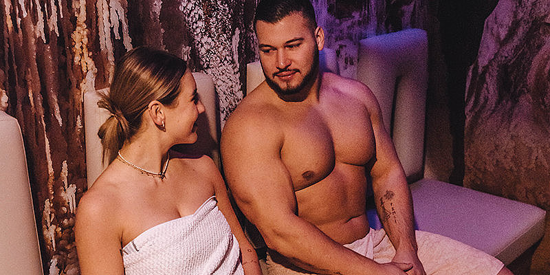 Zwei Personen sitzen in einem Spa-Bereich, entspannt und im Gespräch, umgeben von einer steinernen Wand.