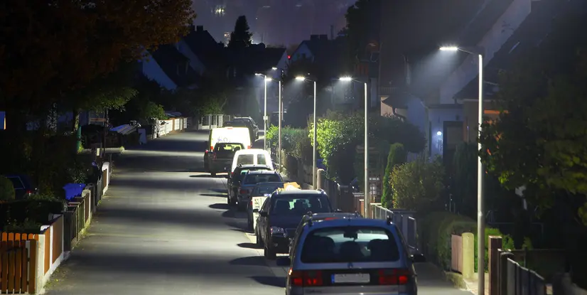 Straßenszene bei Nacht mit beleuchteten Laternen und geparkten Autos in einer ruhigen Wohngegend.
