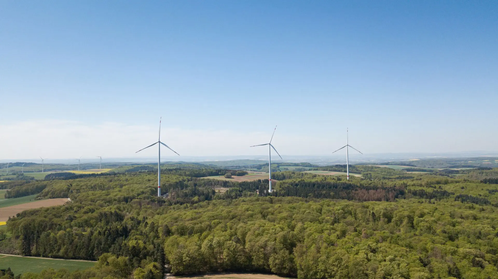 Windkraftanlagen über einer grünen Landschaft unter blauem Himmel.