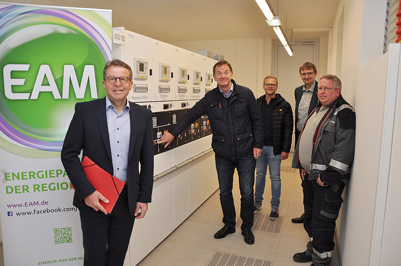 Gruppenfoto von Mitarbeitern der EAM in einem technischen Raum, umgeben von Ausrüstung zur Energieverwaltung.