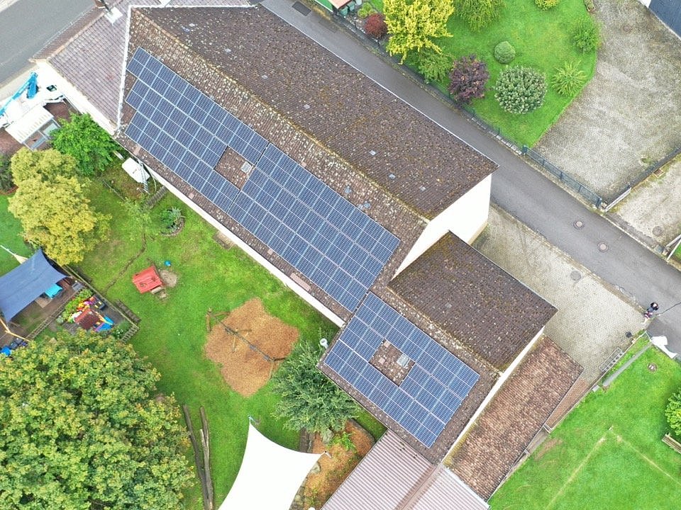 Luftaufnahme von einem Dach eines Einfamilienhauses das auf einer Seite mit PV-Anlagen ausgestattet ist.