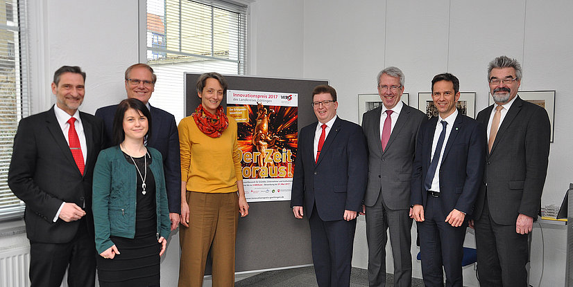 Gruppe von Menschen steht vor einem Plakat des Innovationspreises 2017 des Landkreises Göttingen in einem Büro.