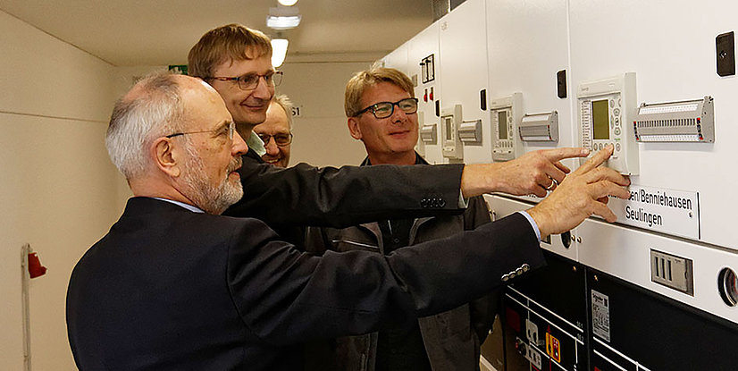 Gruppierung von vier Personen, die gemeinsam an einem Bedienfeld arbeiten und mit verschiedenen Geräten interagieren.