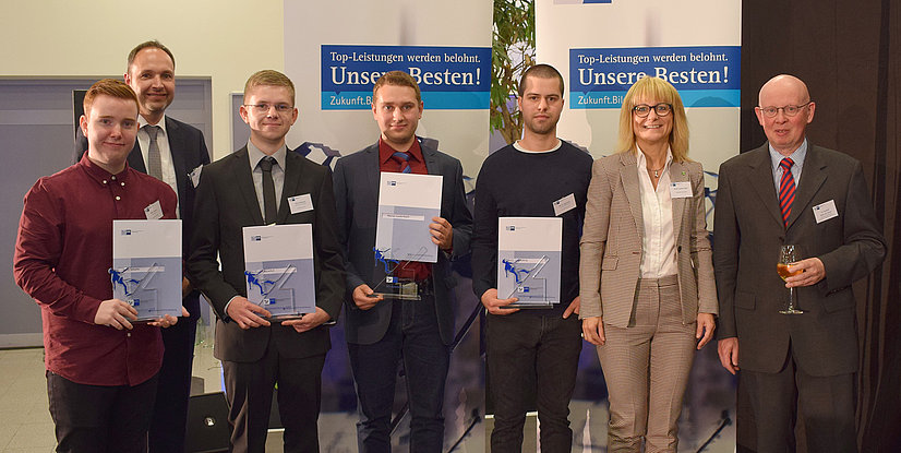 Gruppe von Personen mit Urkunden bei einer Preisverleihung. Hintergrund mit Werbebanner.